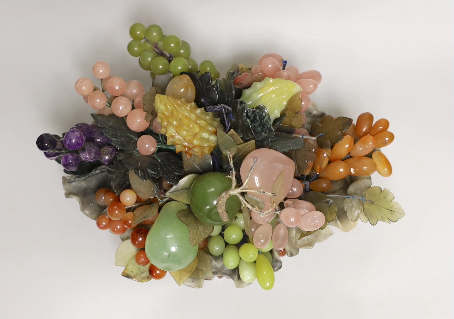 A Chinese soapstone dish of hardstone fruit on hardwood stand, 38cm wide